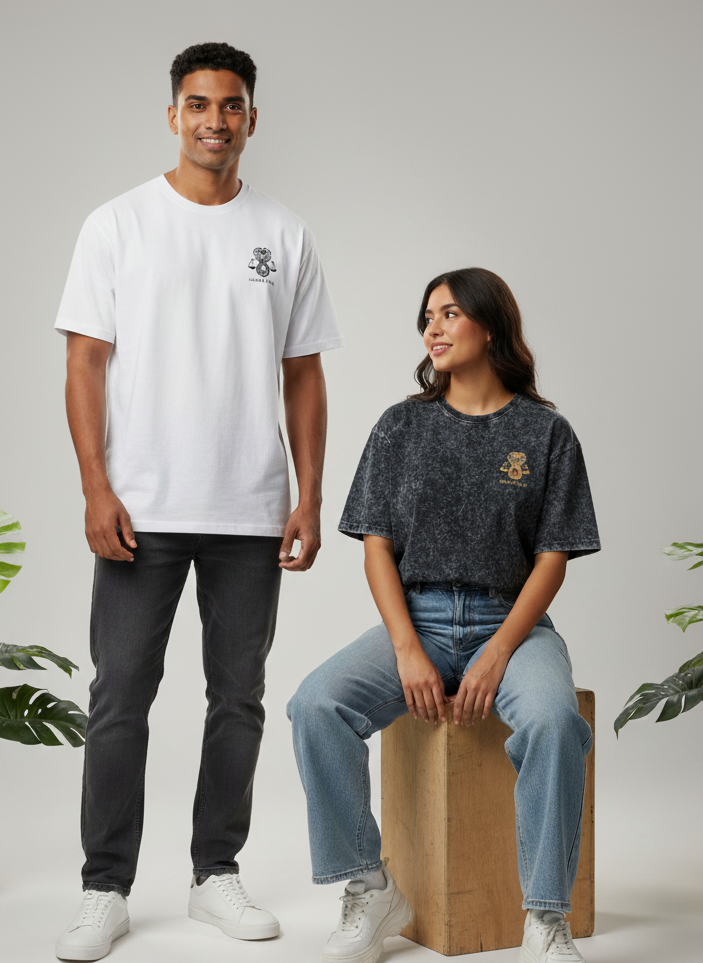 Two people wearing white and black t-shirts with a logo, standing in a minimalistic setting with plants.